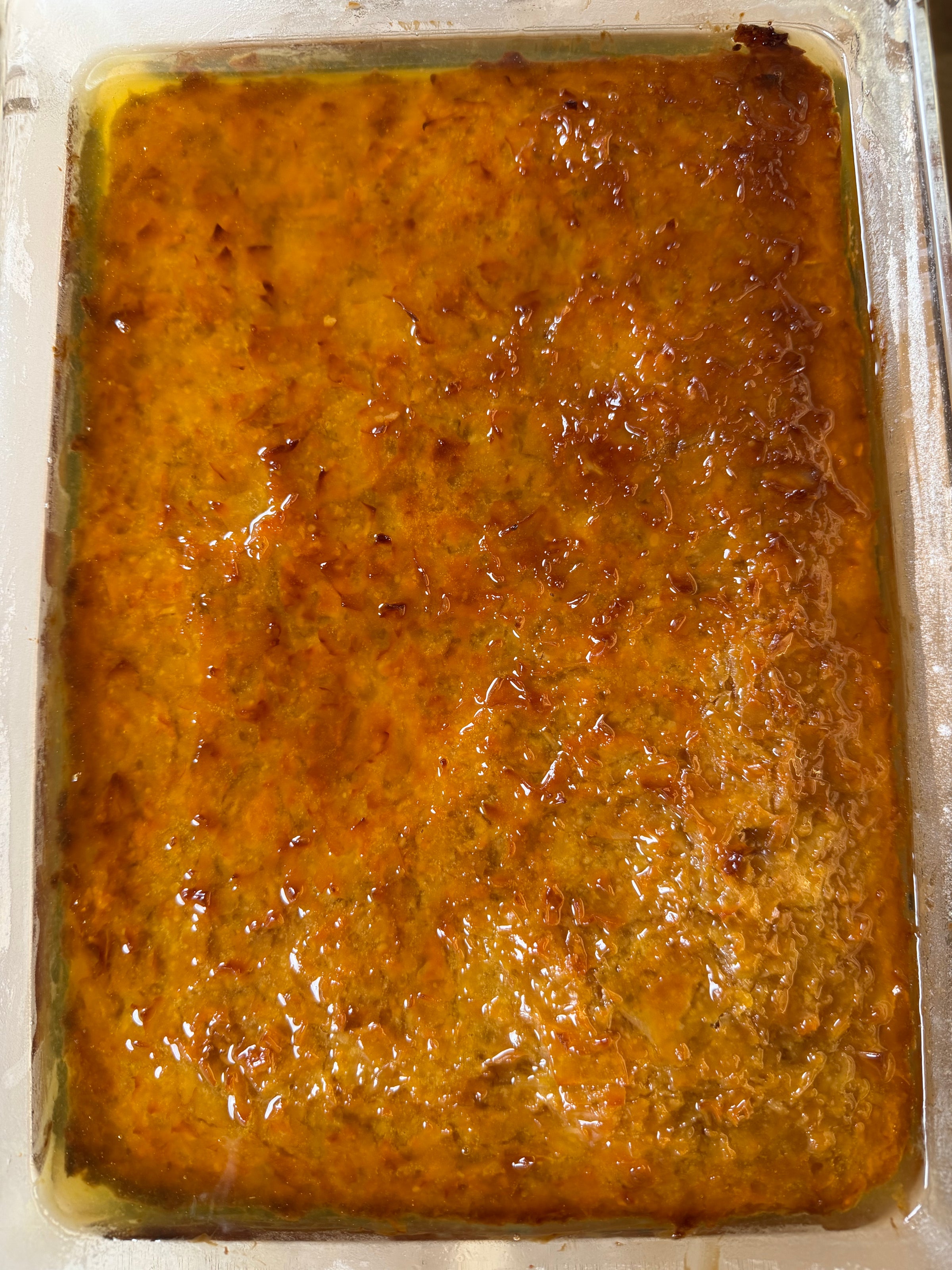 A golden-brown, baked casserole with a shiny, slightly caramelized top layer in a rectangular glass dish.