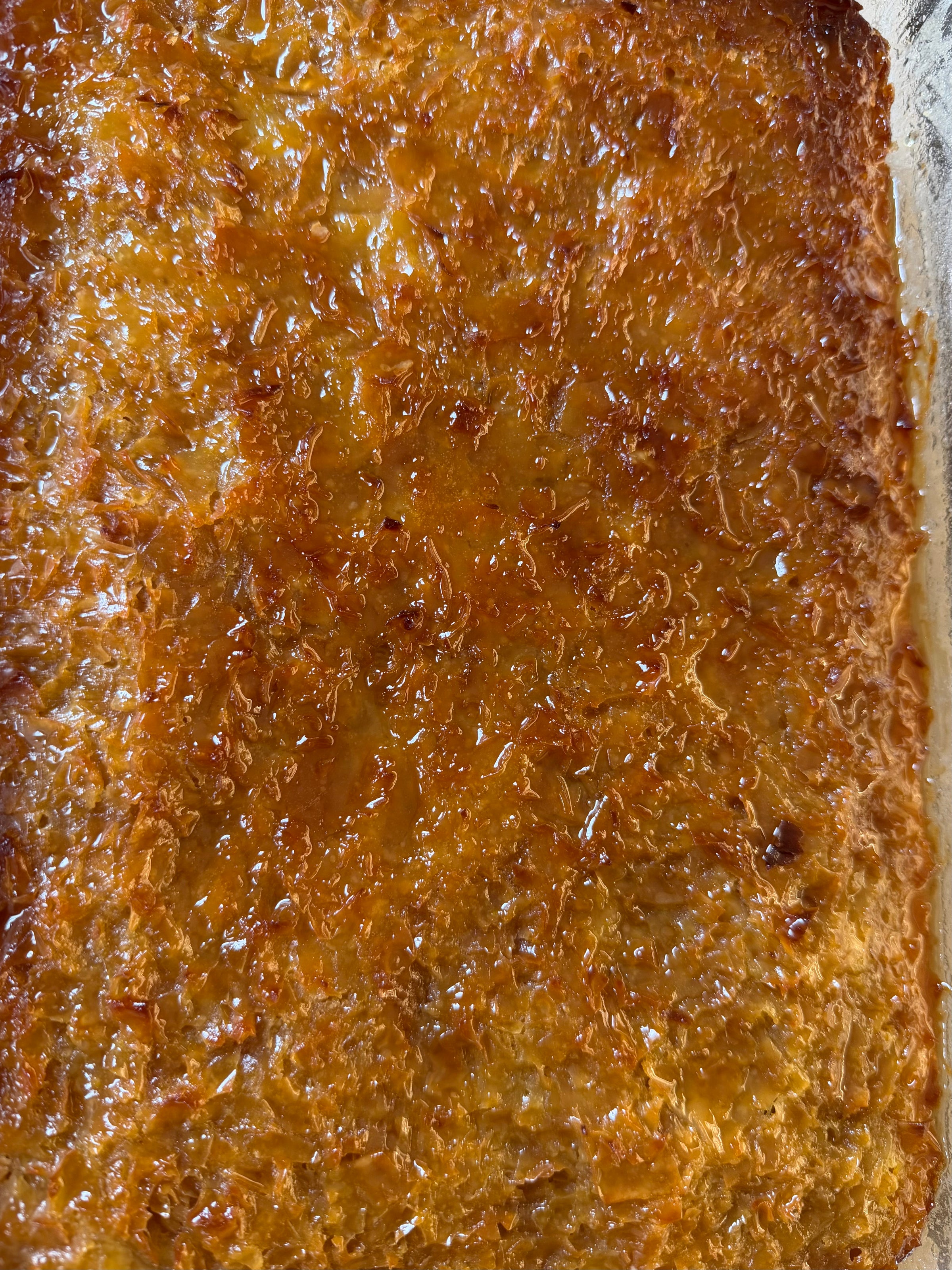 Close-up of a golden-brown, caramelized, and crispy baked surface, possibly a dessert like leche flan or cassava cake, showing a shiny, textured, and slightly bubbly appearance.