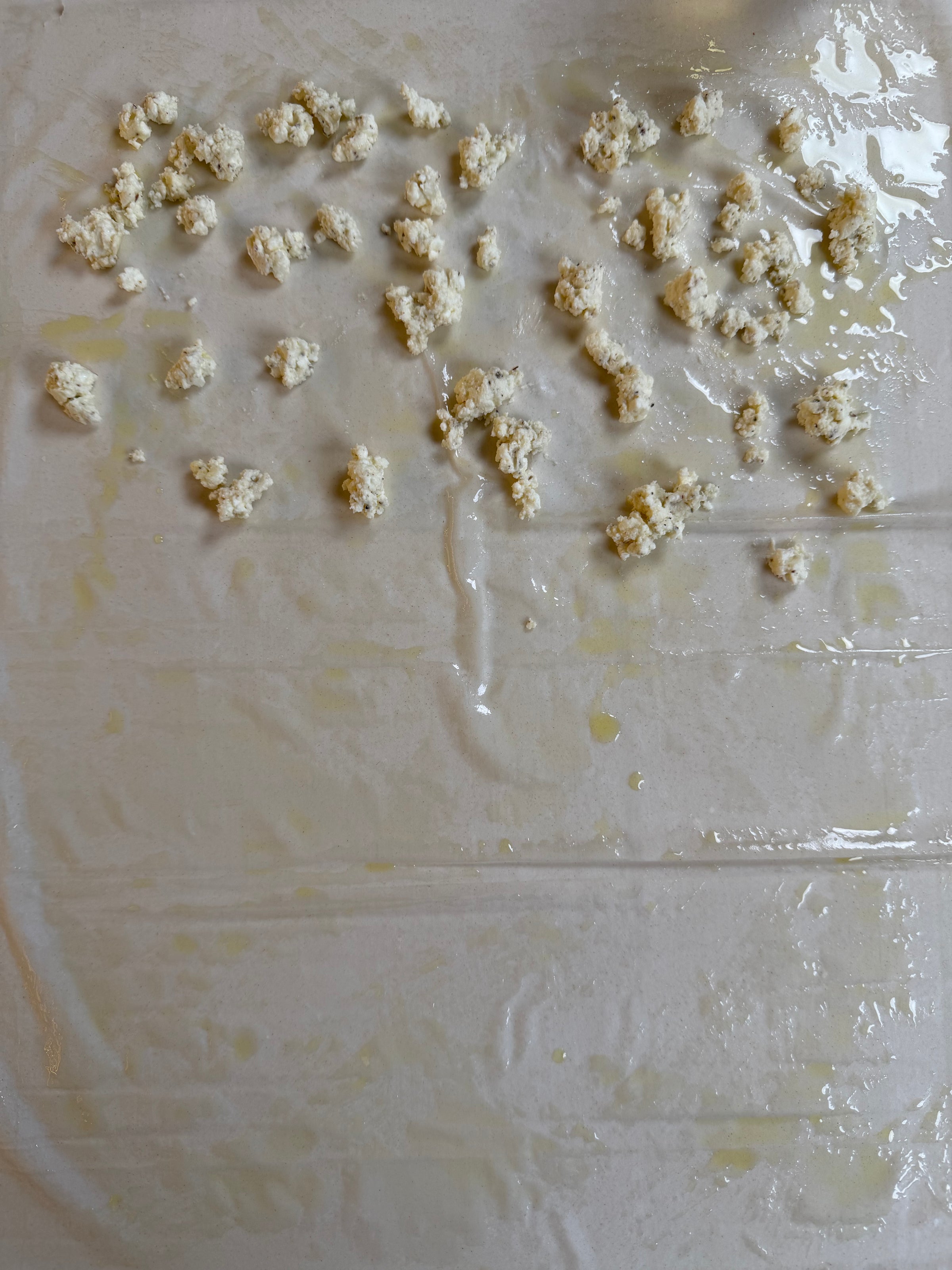 Crumbled cheese is scattered on thin, translucent sheets of dough brushed with oil, likely phyllo pastry, spread out on a flat surface.