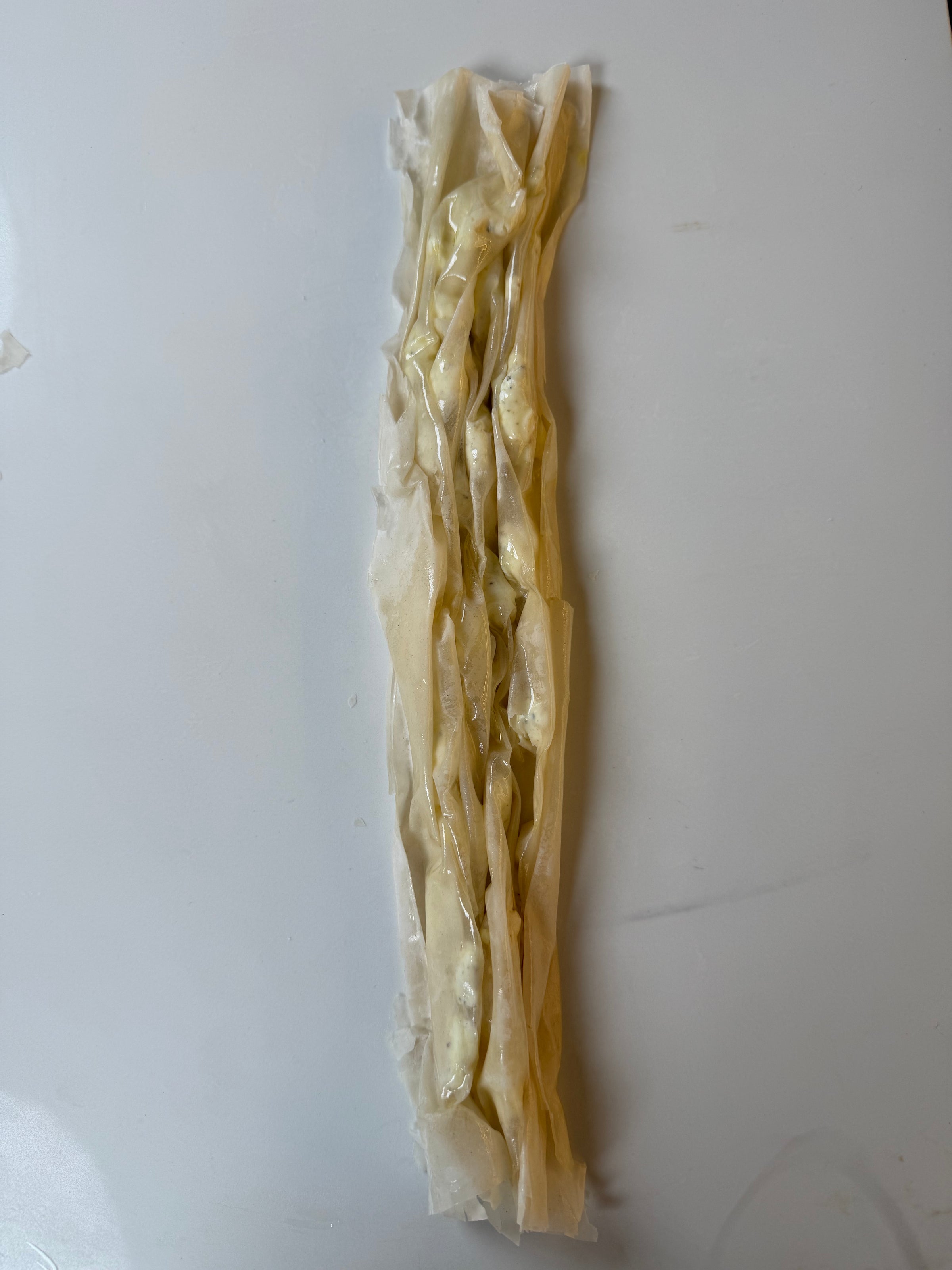 A long, narrow strip of crumpled parchment paper with a light yellow substance inside, placed on a plain white surface.