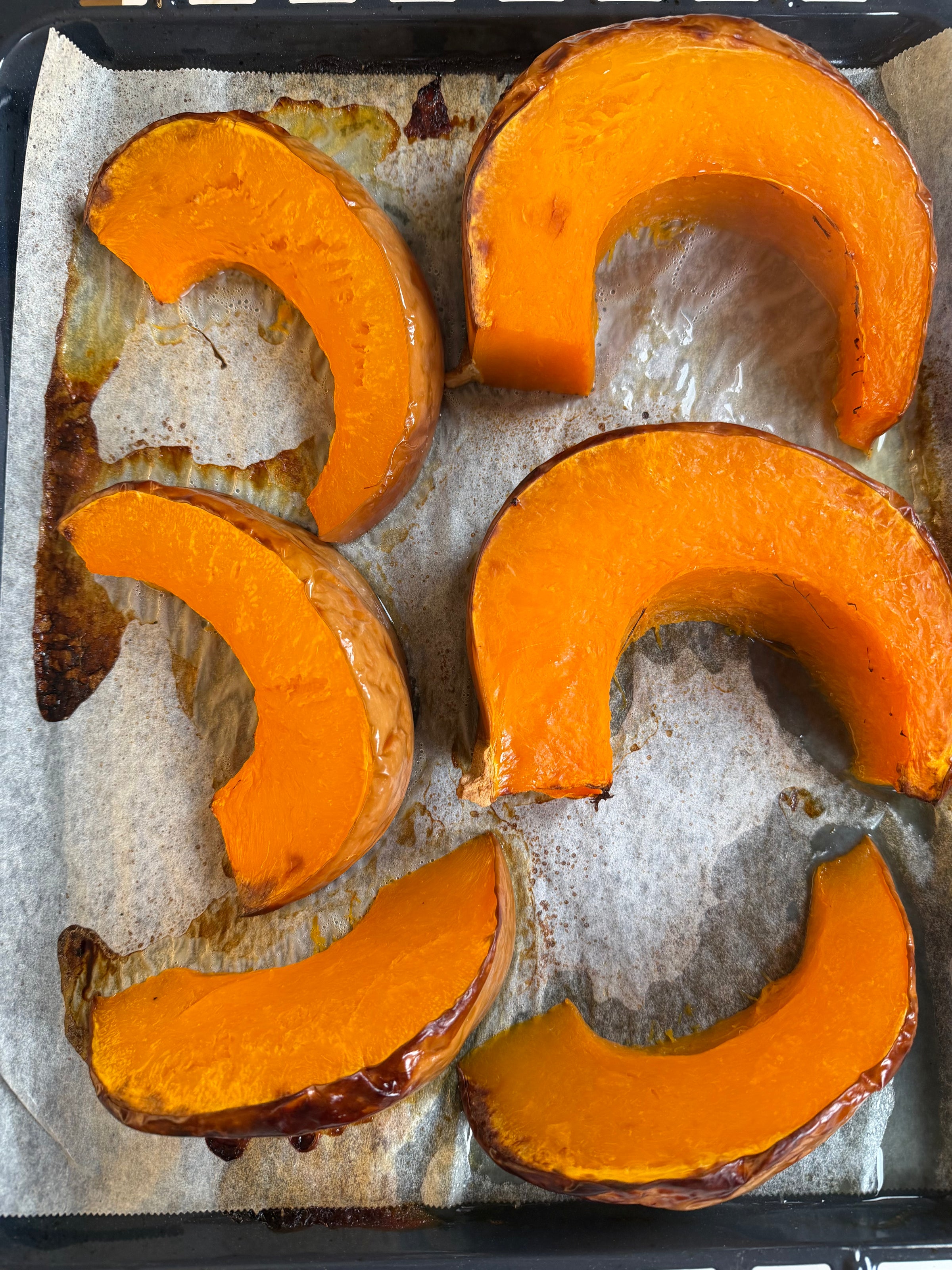 Five roasted pumpkin wedges on a parchment-lined baking sheet.