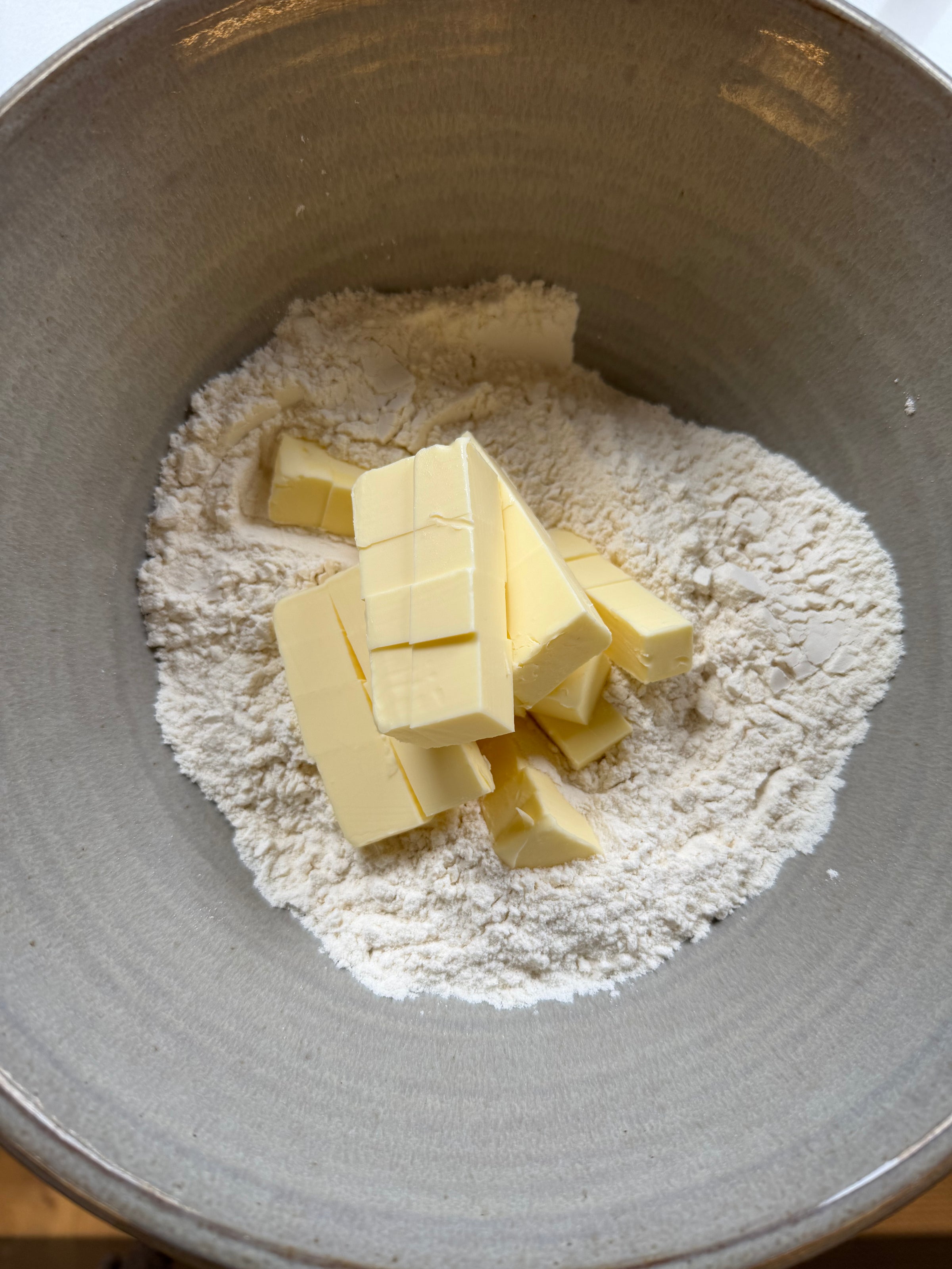 A pile of cubed butter resting on a bed of flour in a ceramic bowl.