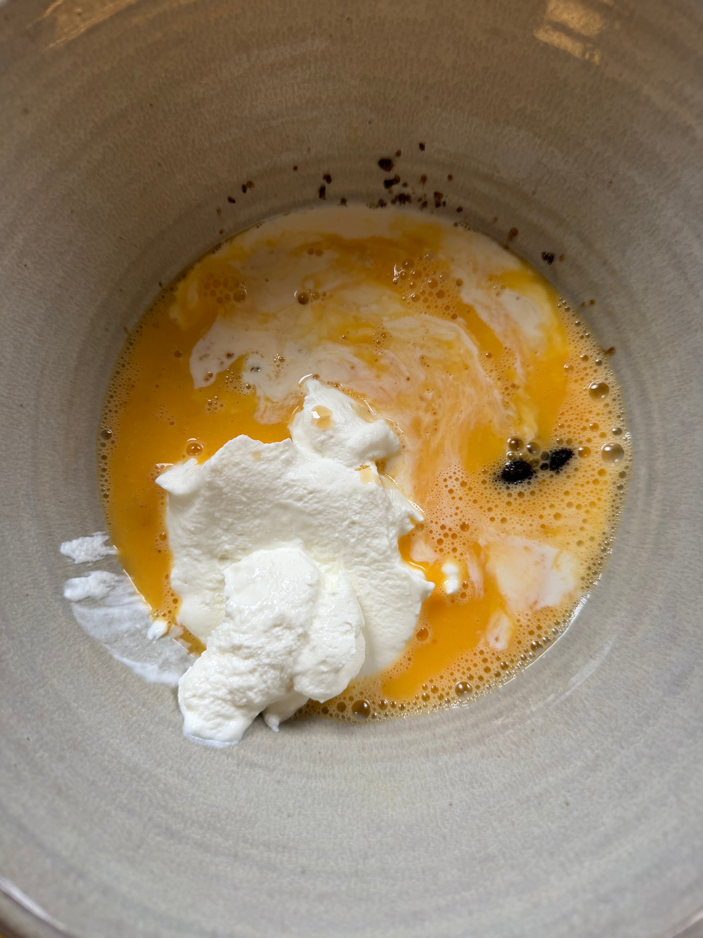 A ceramic bowl containing beaten eggs mixed with cream and a dollop of sour cream.