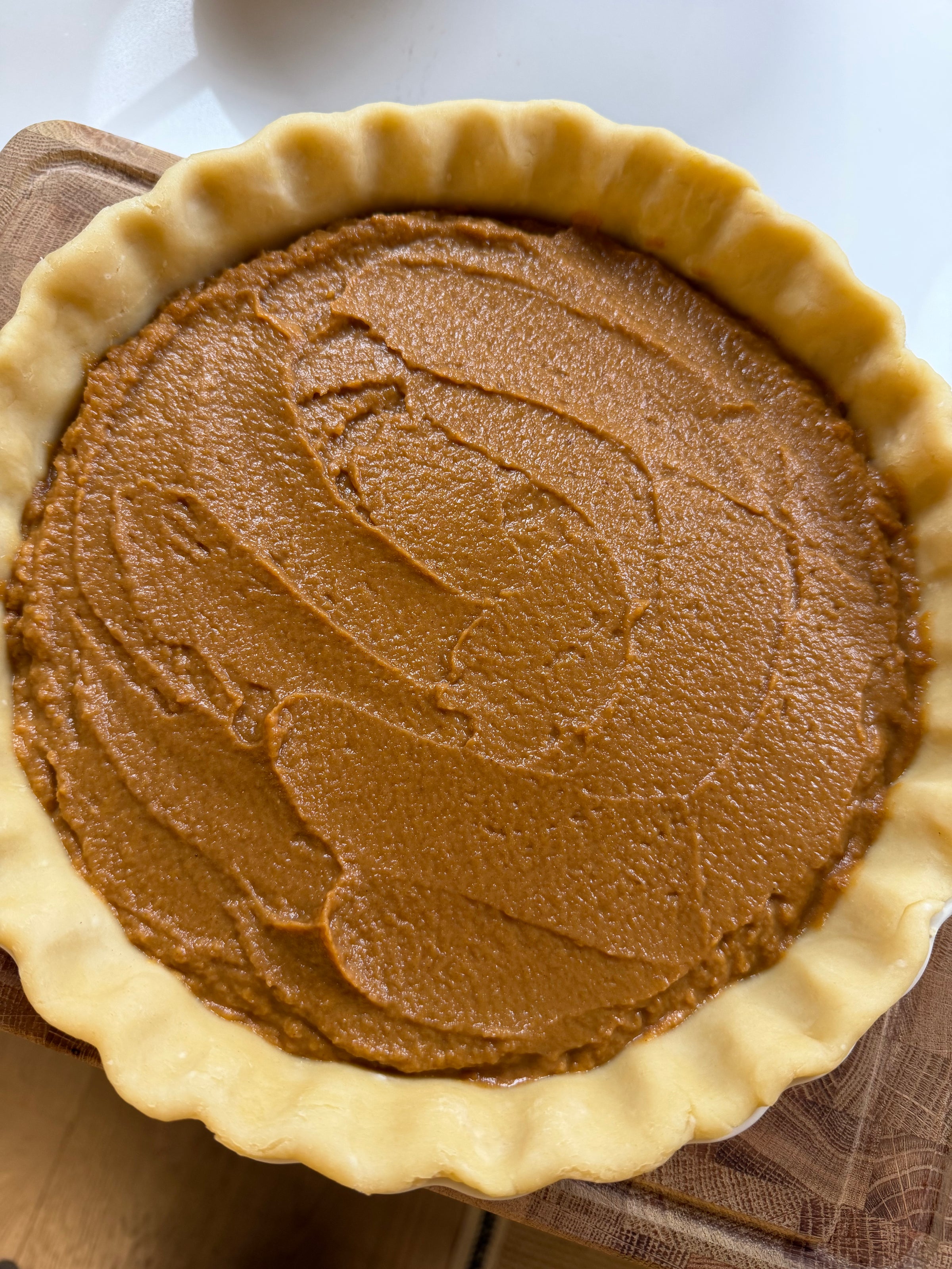 An unbaked pumpkin pie in a crimped pastry crust on a wooden board.
