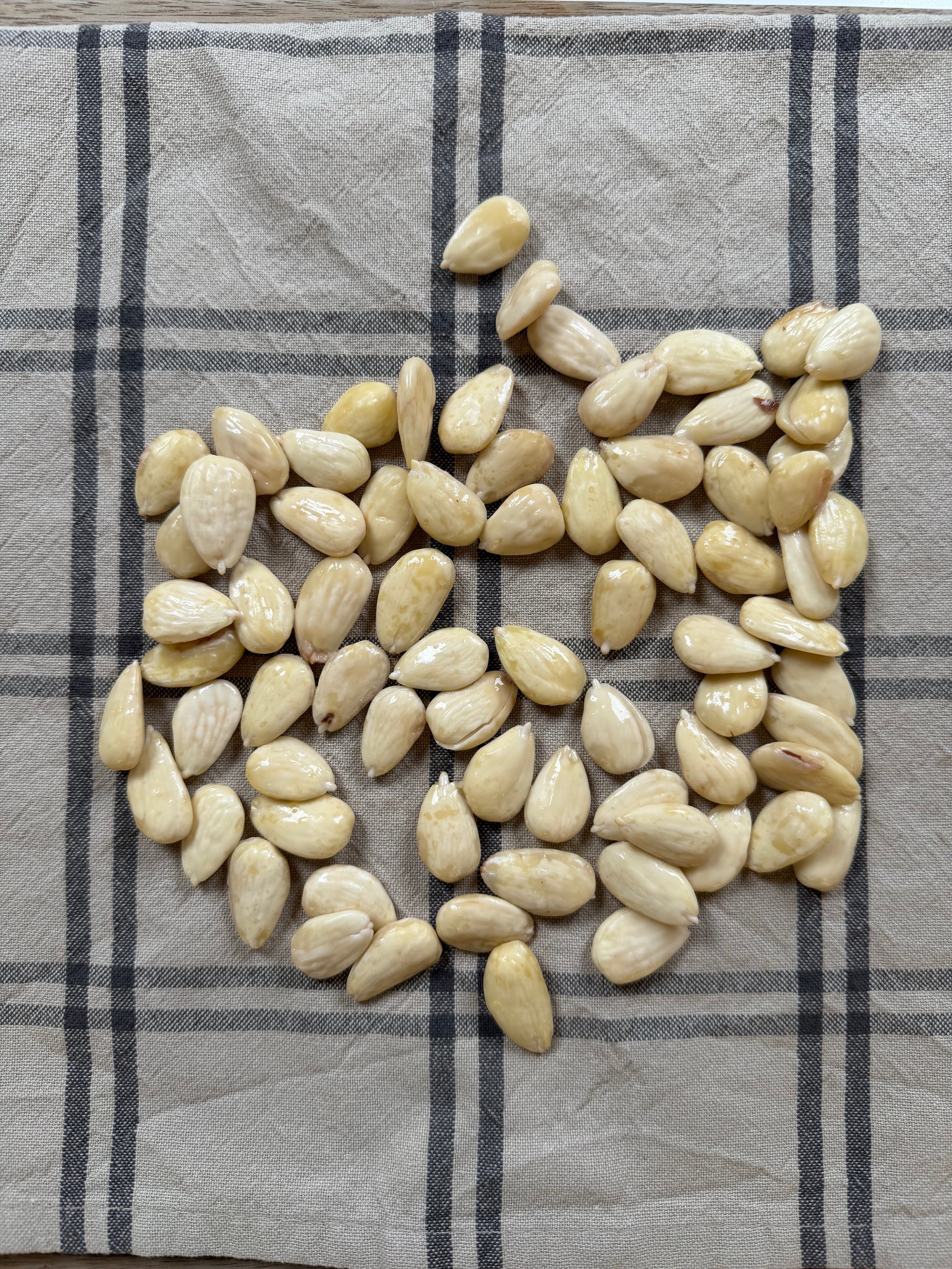 A pile of peeled almonds spread out on a beige cloth with a gray and black plaid pattern.