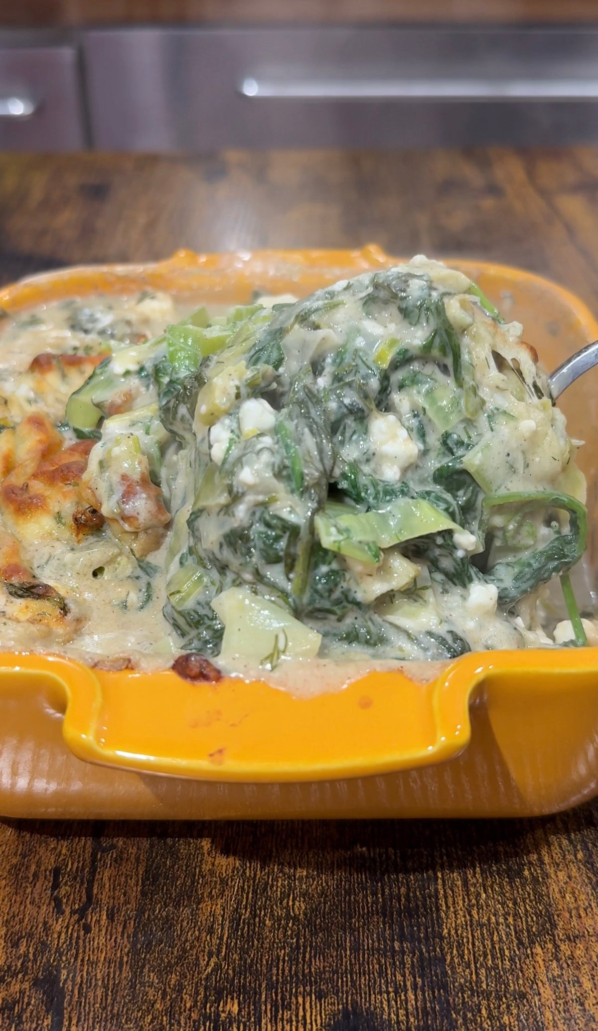A spoonful of creamy spinach and cheese dip being lifted from an orange ceramic baking dish.