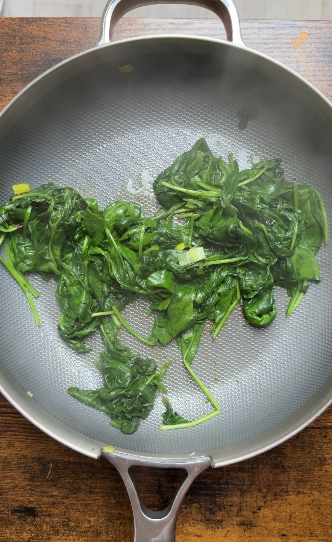 Spinach wilting in a non-stick skillet with bits of chopped green onion.
