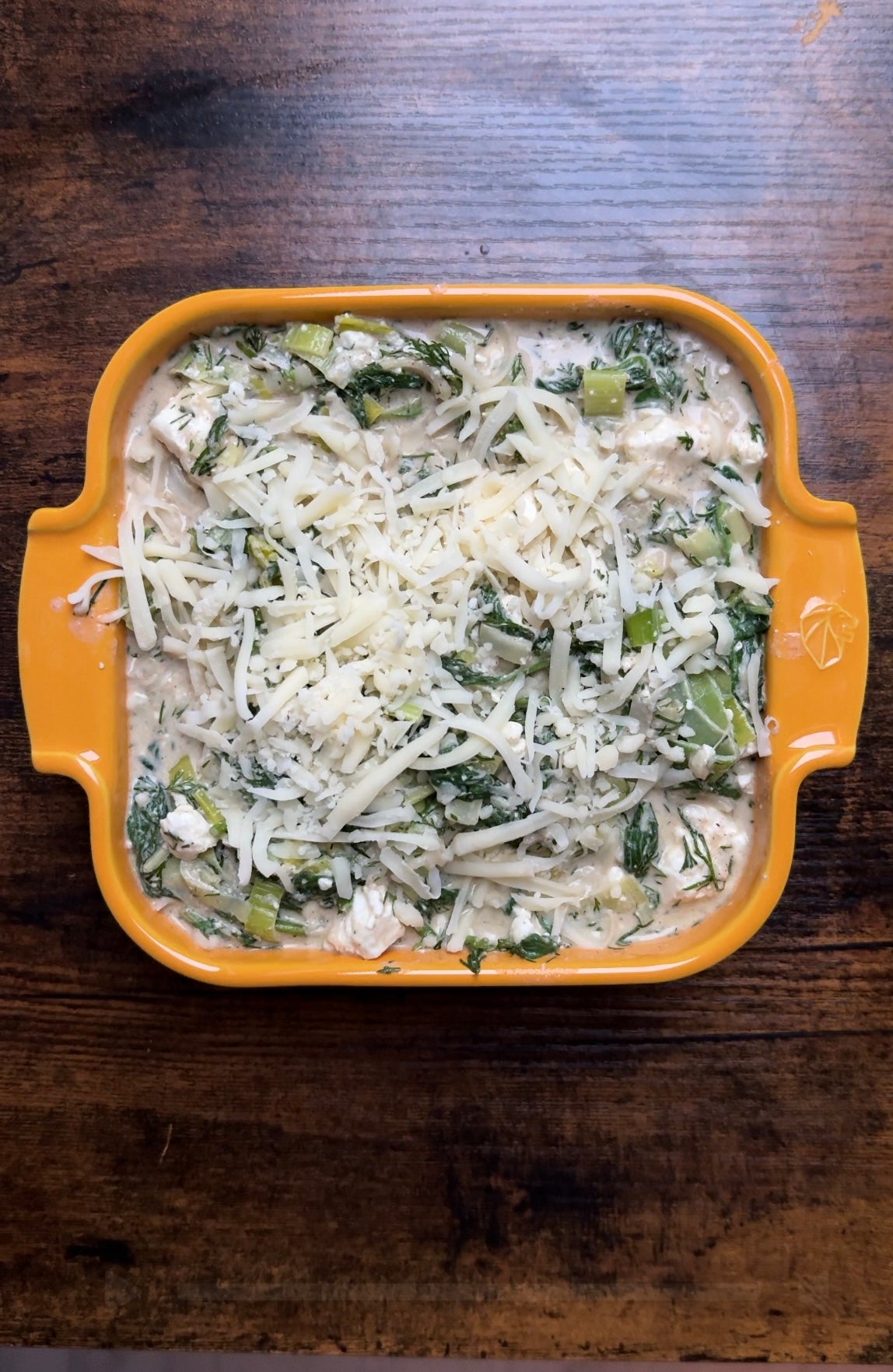 A creamy chicken and spinach casserole topped with shredded cheese in a square orange baking dish.