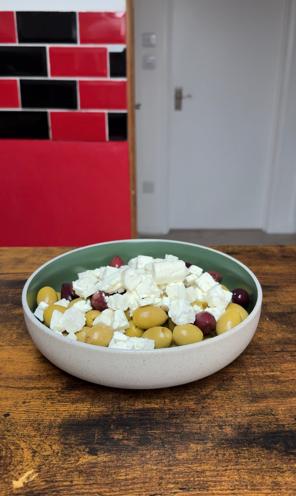 A bowl filled with green and dark olives topped with crumbled feta cheese.