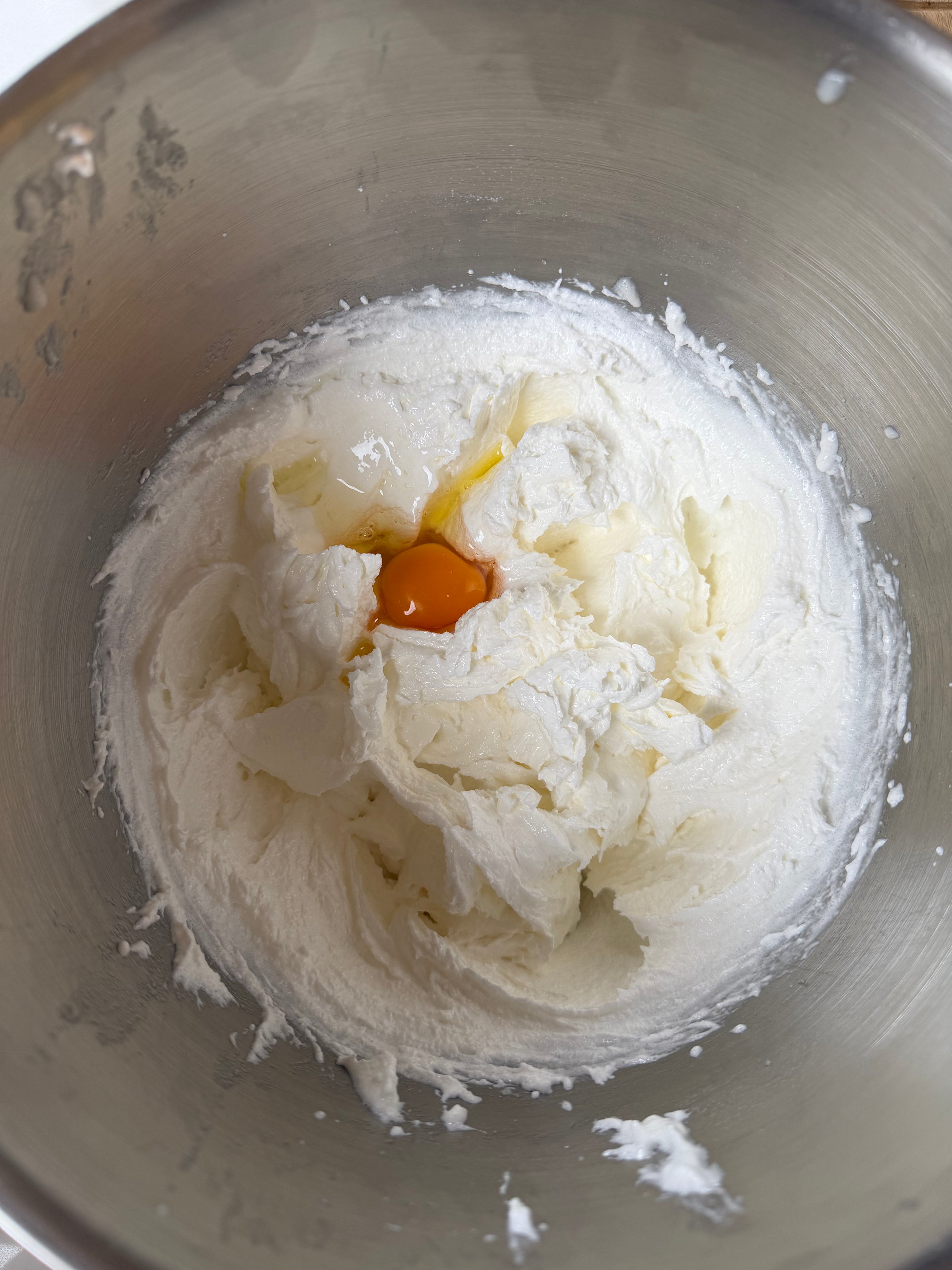 A metal mixing bowl containing creamed butter and sugar with a raw egg cracked in the center, ready to be mixed.