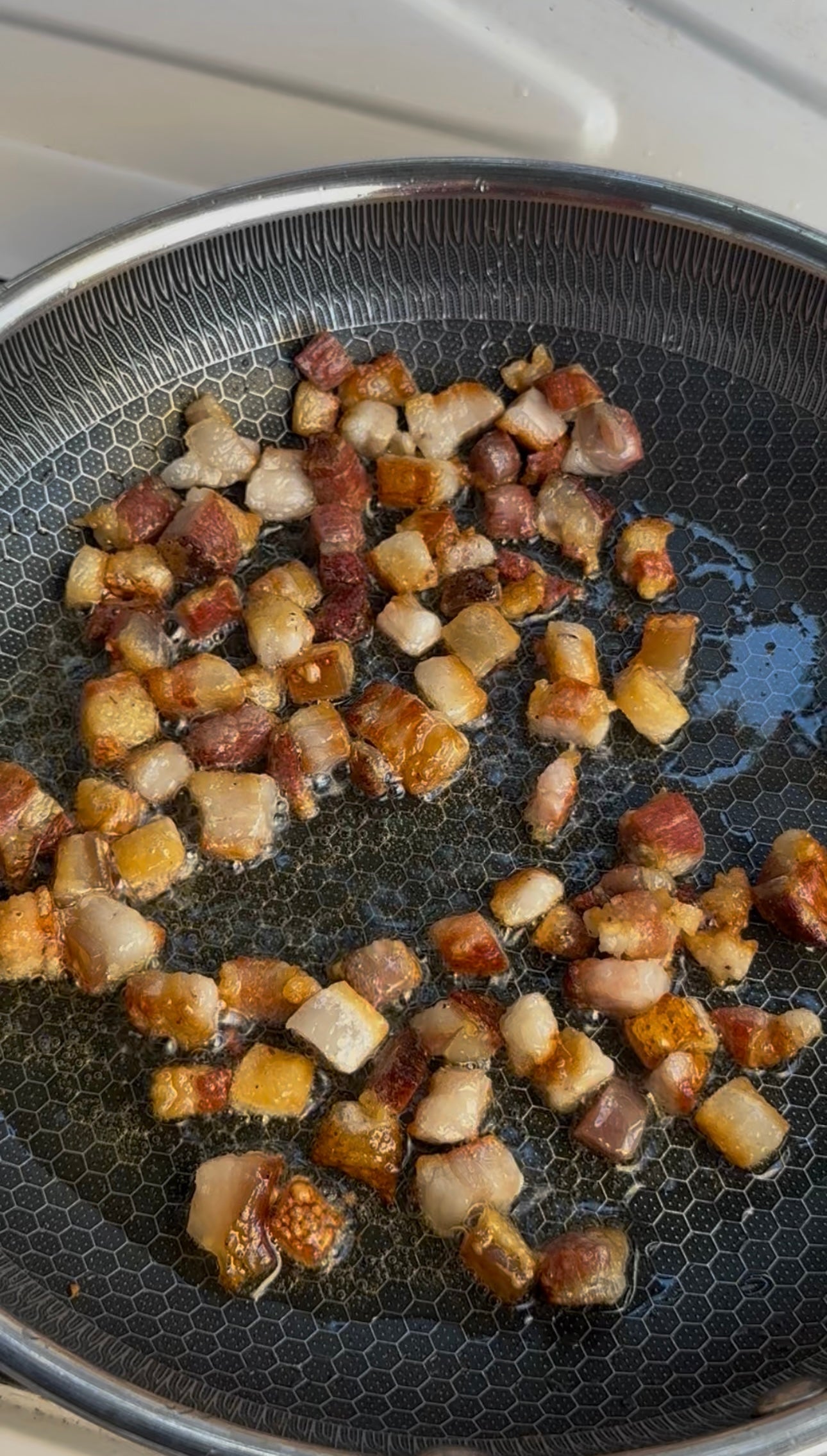Small cubes of pork belly are frying in oil in a nonstick pan, turning golden brown and crispy.