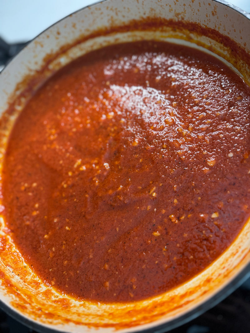 A close-up of a pot filled with thick, red tomato sauce, with visible bits of garlic or onion and a slightly glossy surface.