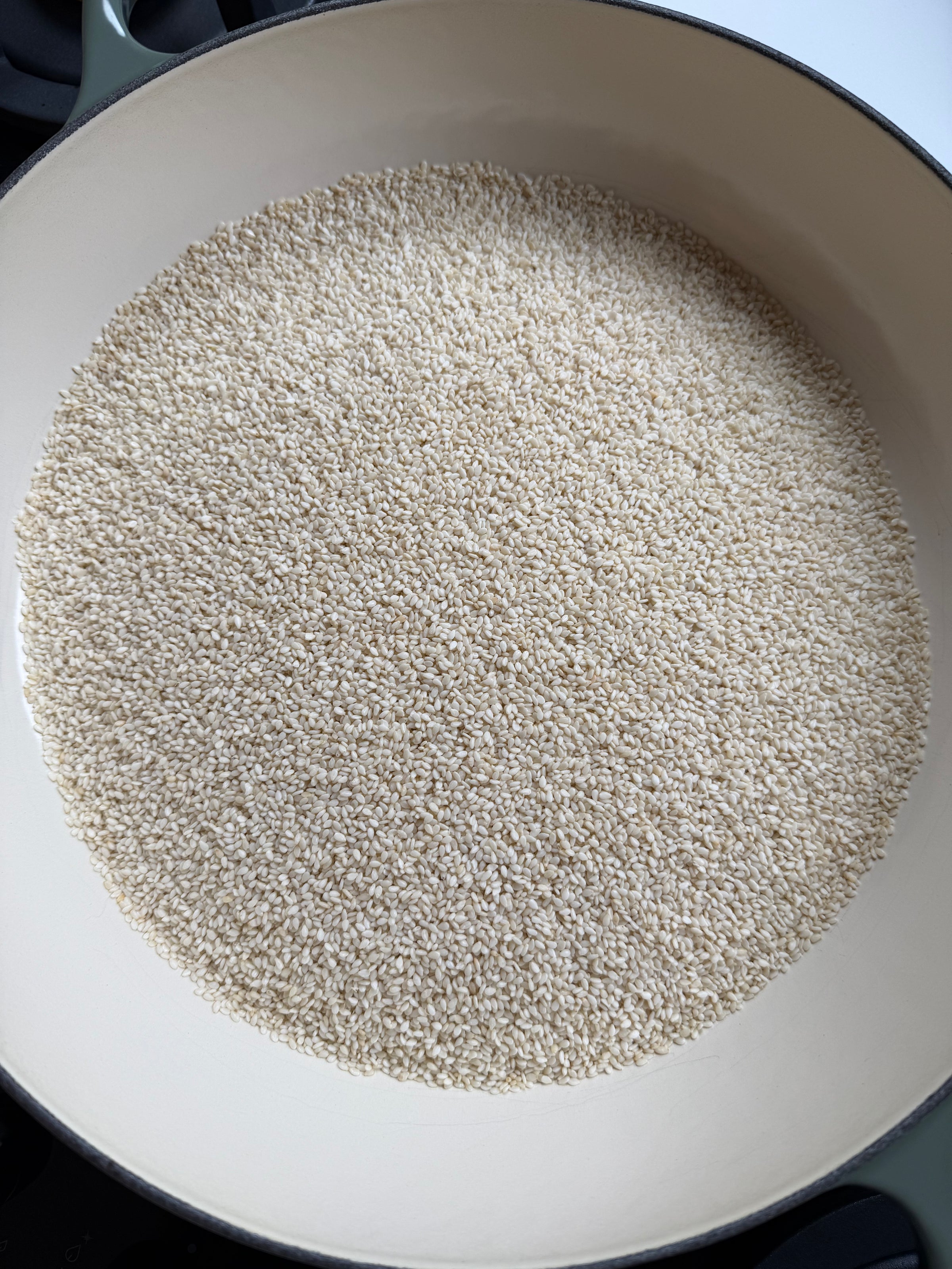 A large, off-white ceramic pan filled with an even layer of uncooked sesame seeds.