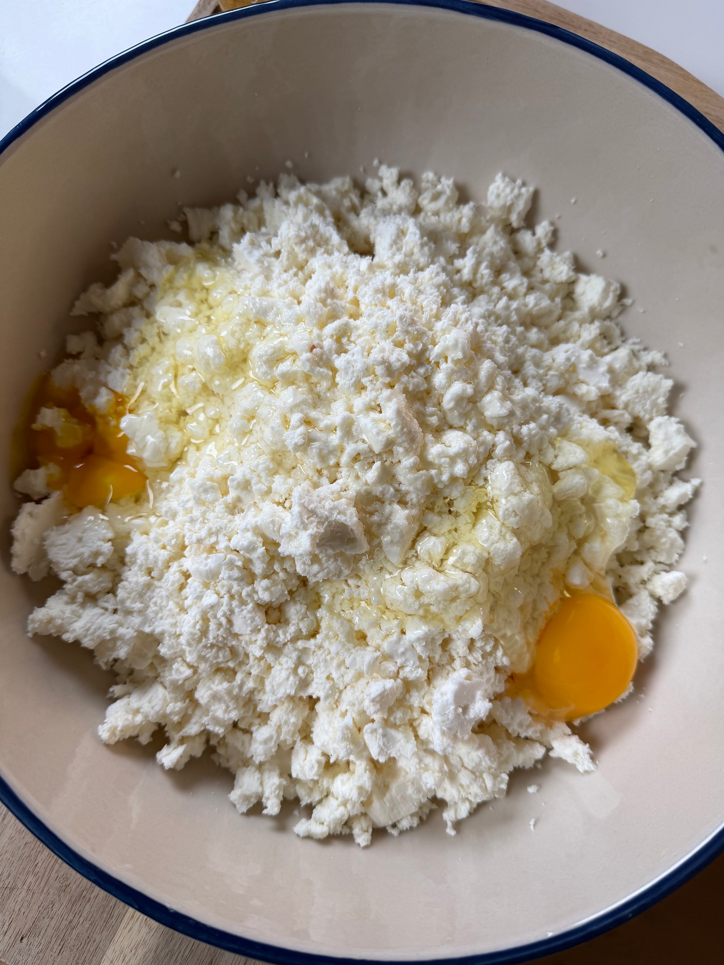 A mixing bowl containing crumbled white cheese and two cracked eggs with visible yolks, ready to be mixed together.