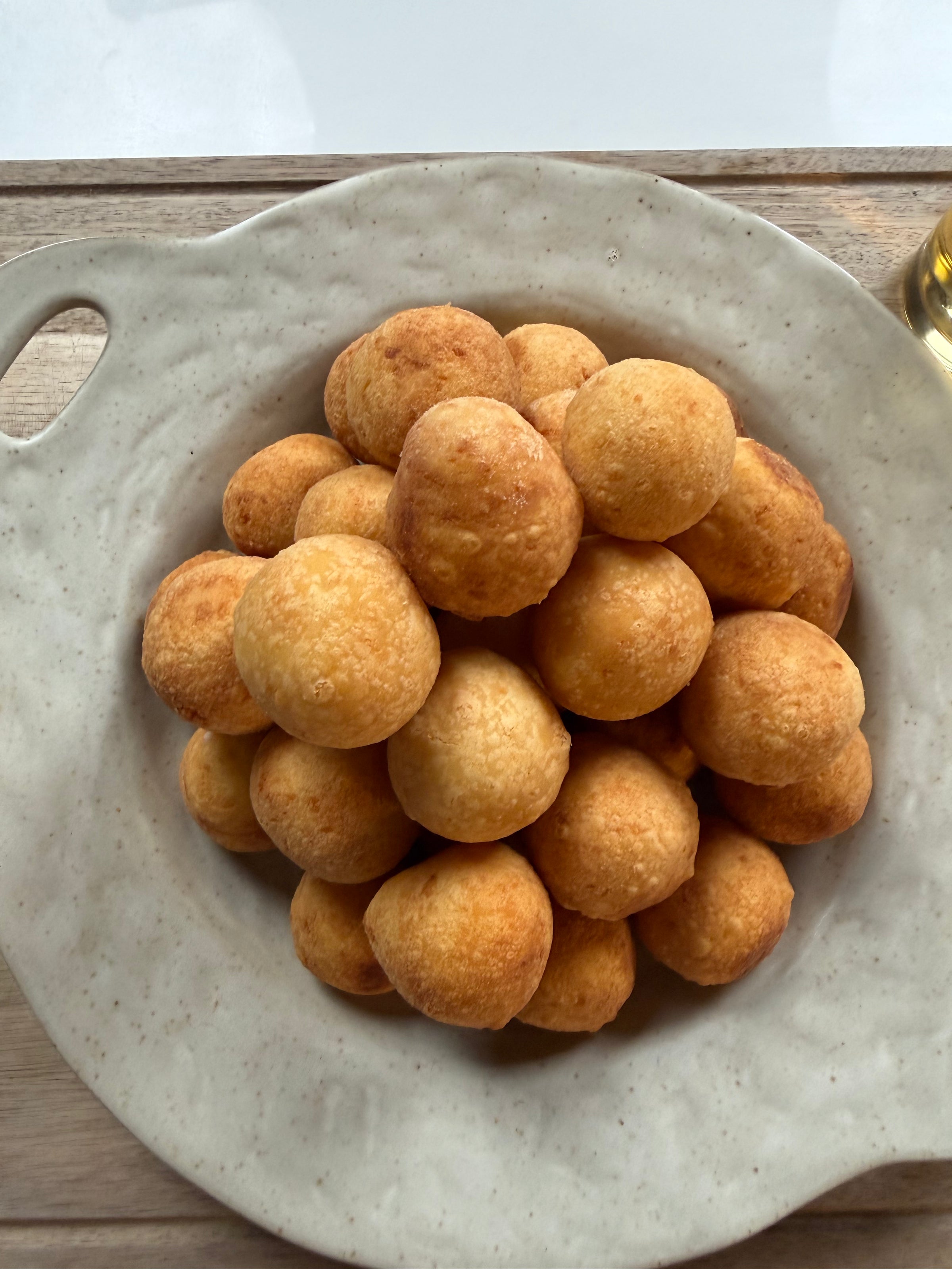 A pile of round, golden-brown cheese bread balls arranged on a speckled ceramic plate with a handle, placed on a wooden surface.