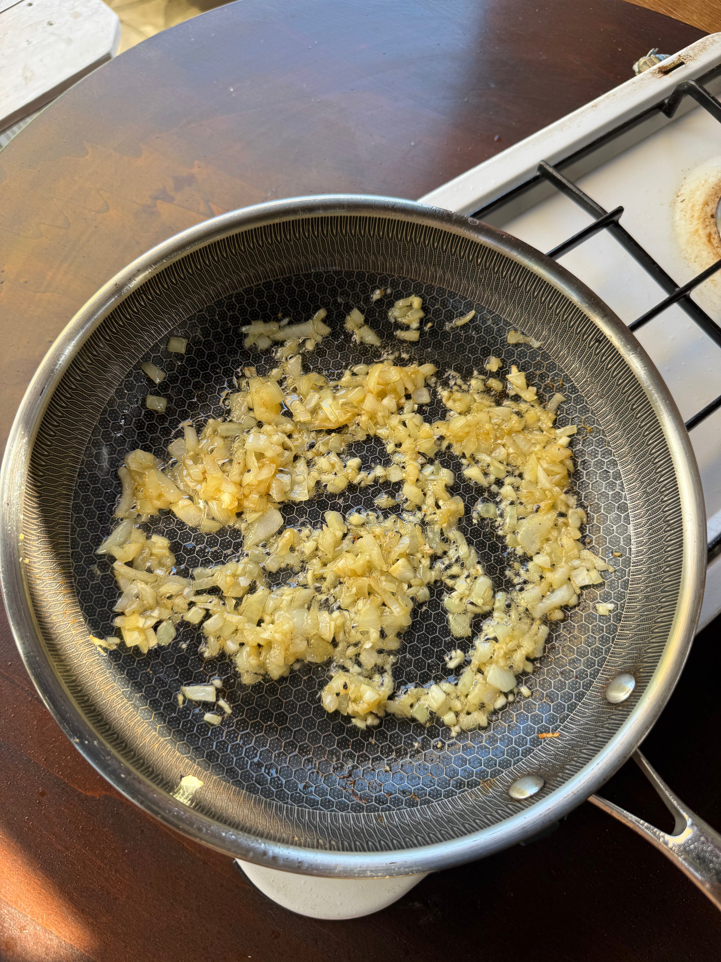 Chopped onions and garlic are sautéing in a frying pan on a stovetop, beginning to turn golden brown.