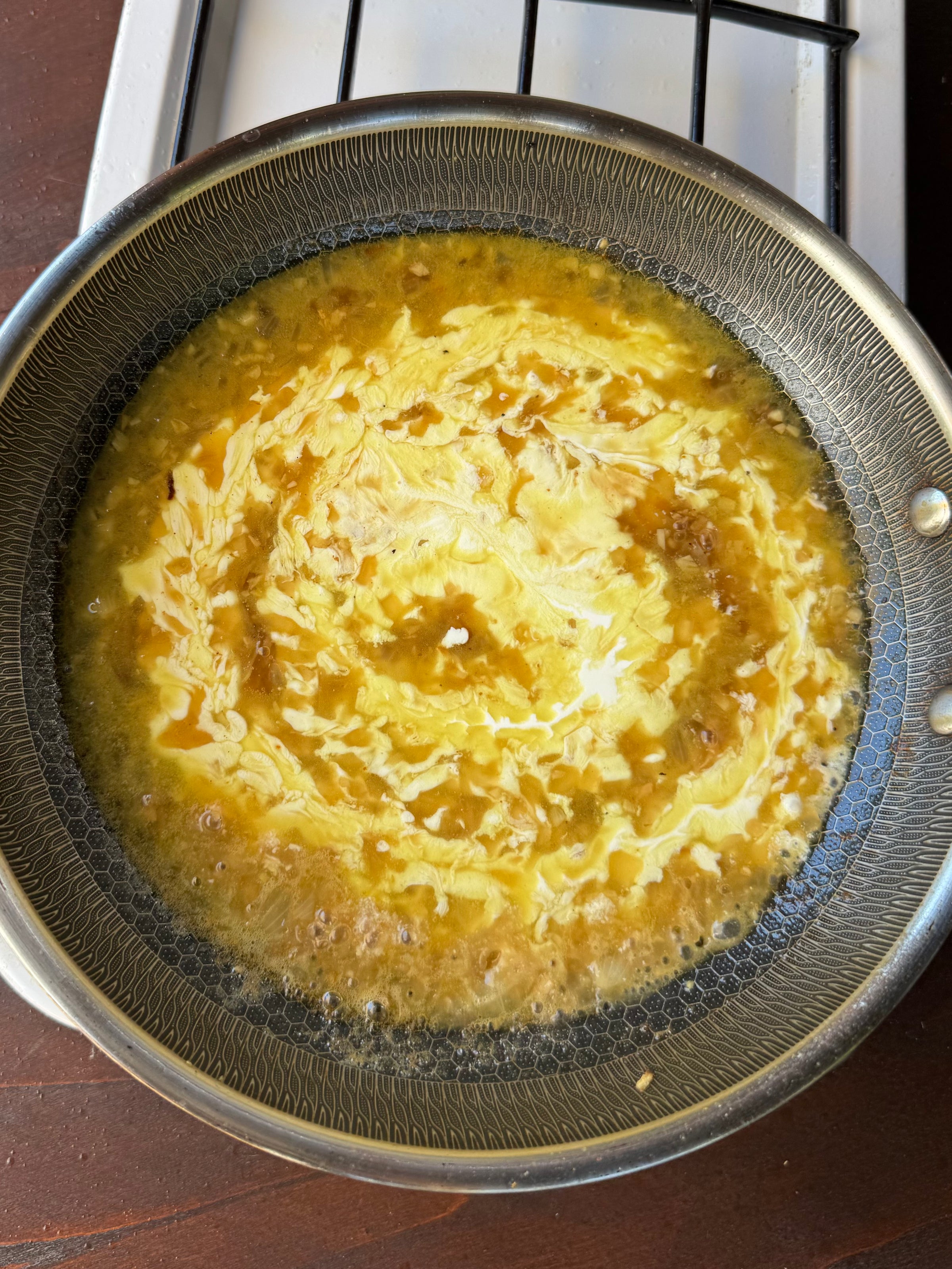 Eggs cooking in a frying pan on a stovetop, with the yolk and white swirling together, beginning to set but still partially liquid.