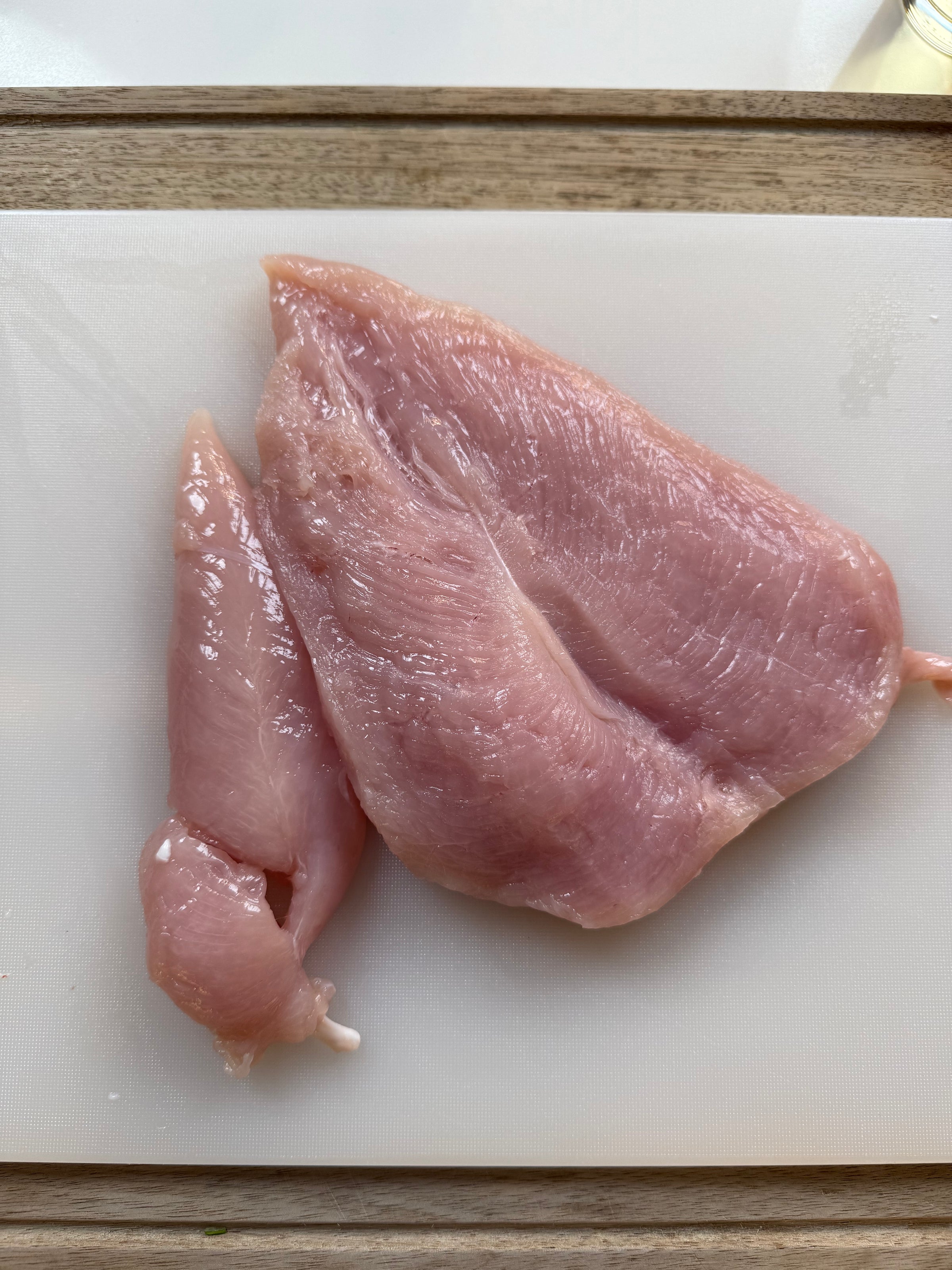 Raw, boneless chicken breast and tenderloin placed on a white cutting board, ready for preparation or cooking. The meat is light pink and unseasoned.