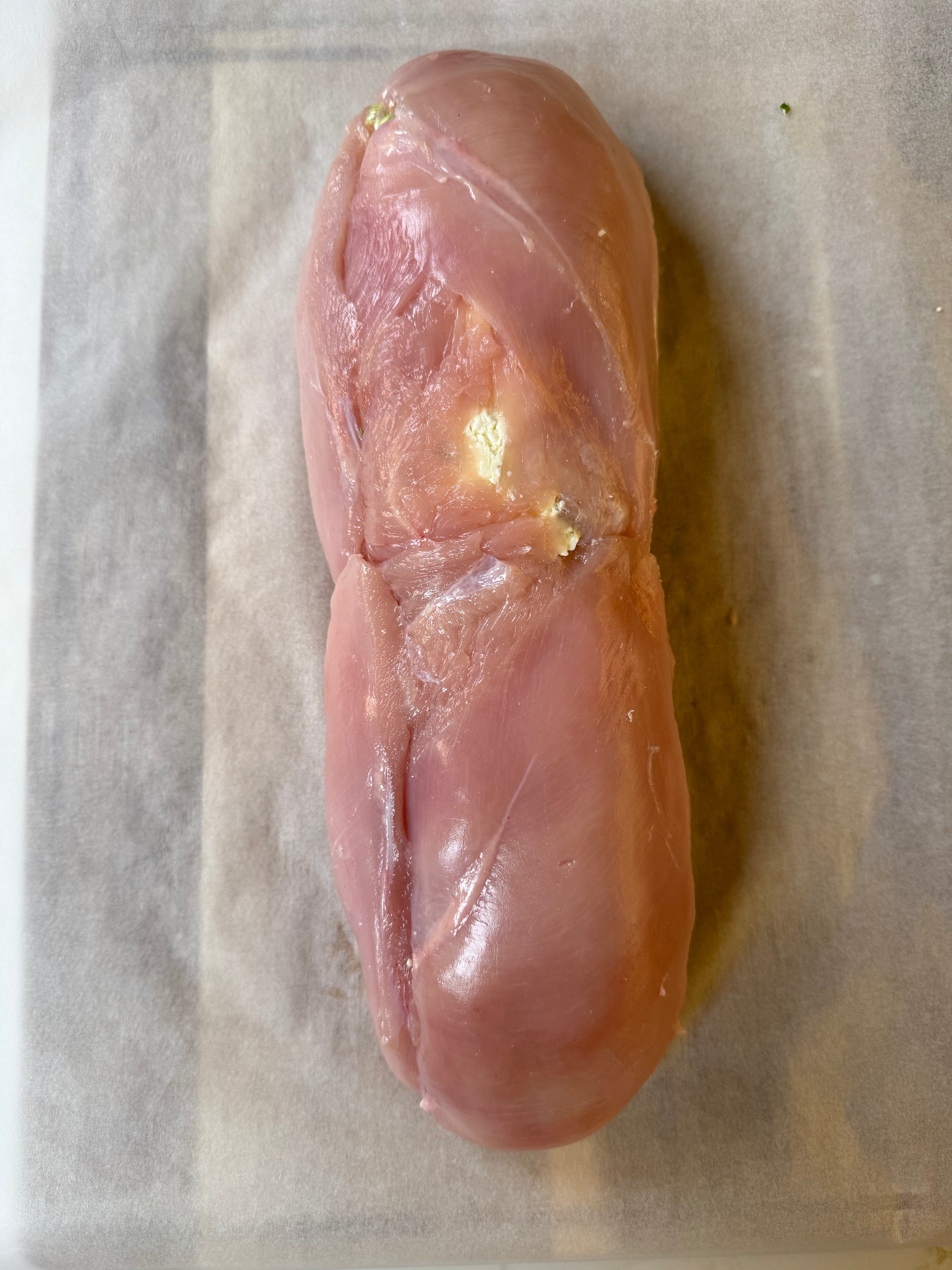 Raw, boneless, skinless chicken breast tied with kitchen twine, placed on a sheet of parchment paper.