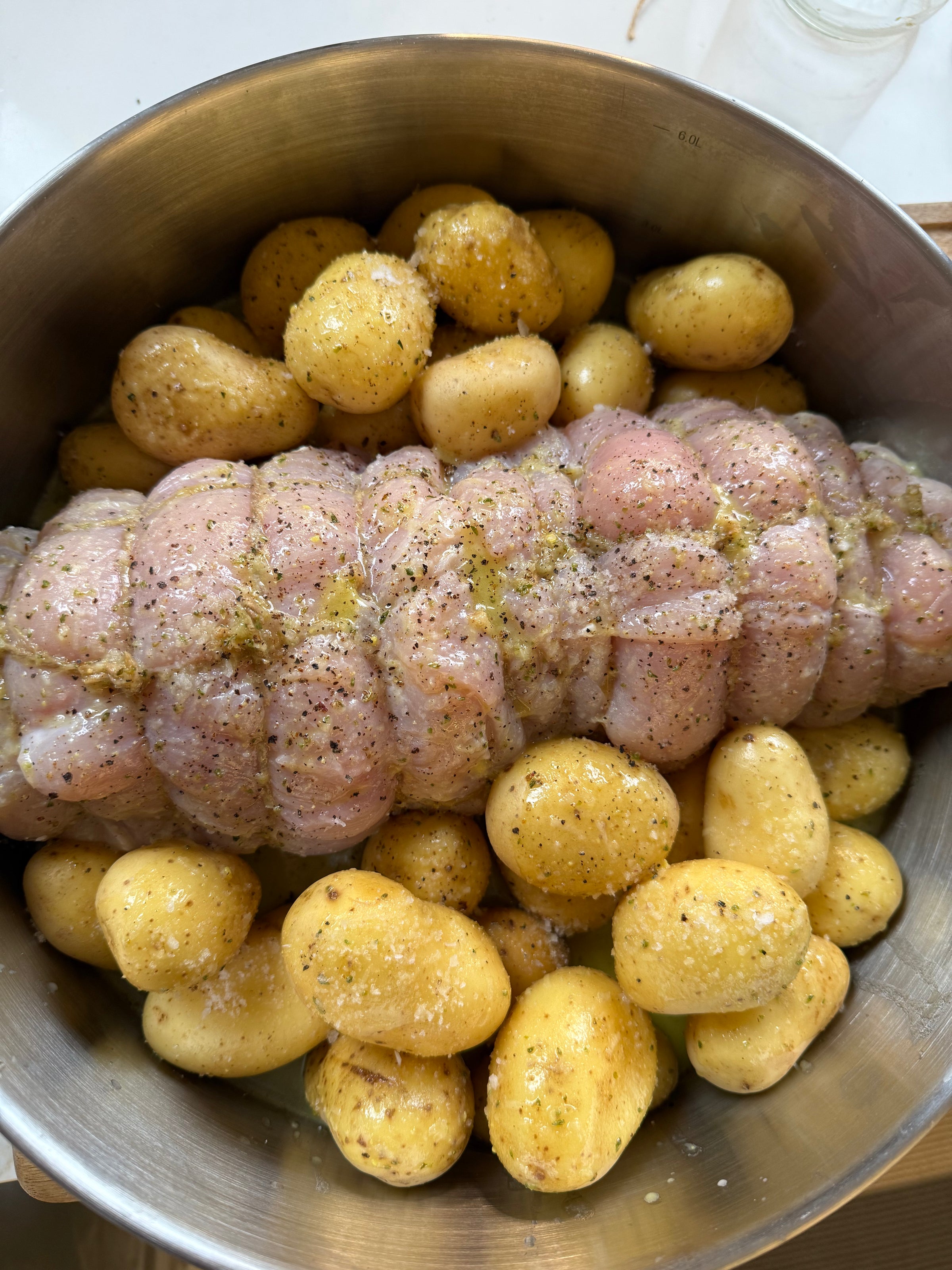 Uncooked pork roast tied with string, seasoned with pepper and salt, surrounded by small yellow potatoes in a metal baking dish.