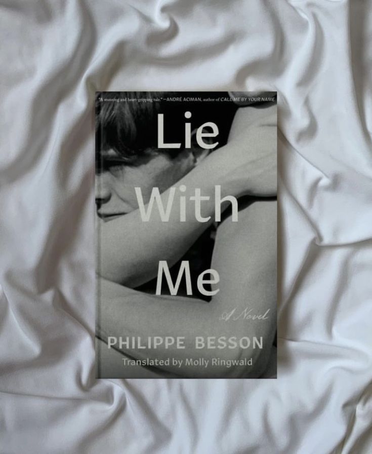 A black-and-white book cover titled Lie With Me by Philippe Besson, translated by Molly Ringwald, lies on white, crumpled fabric. The cover shows a close-up of two people embracing.