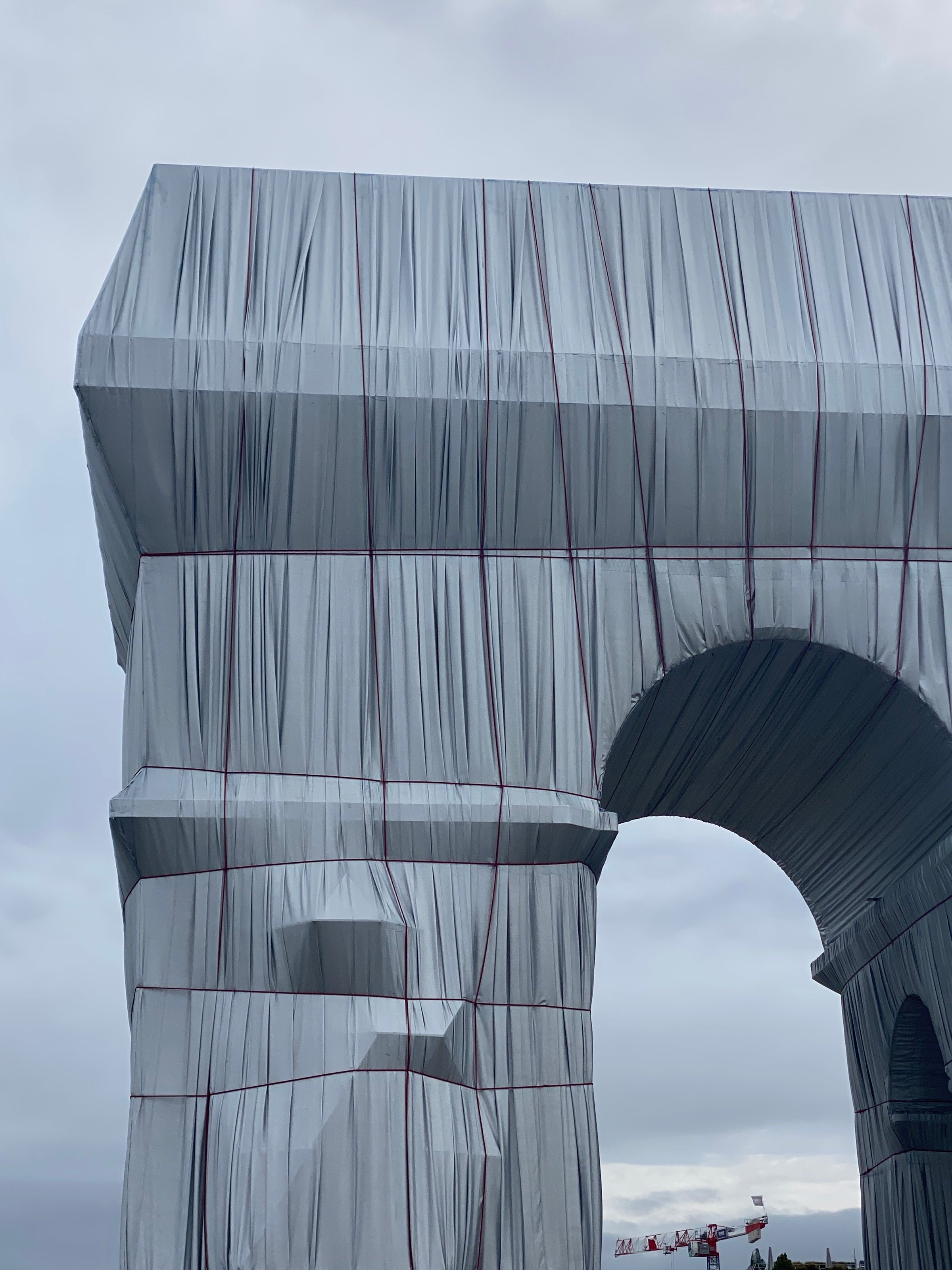 The Arc de Triomphe in Paris covered in silver fabric and red rope as part of an art installation, set against a cloudy sky.