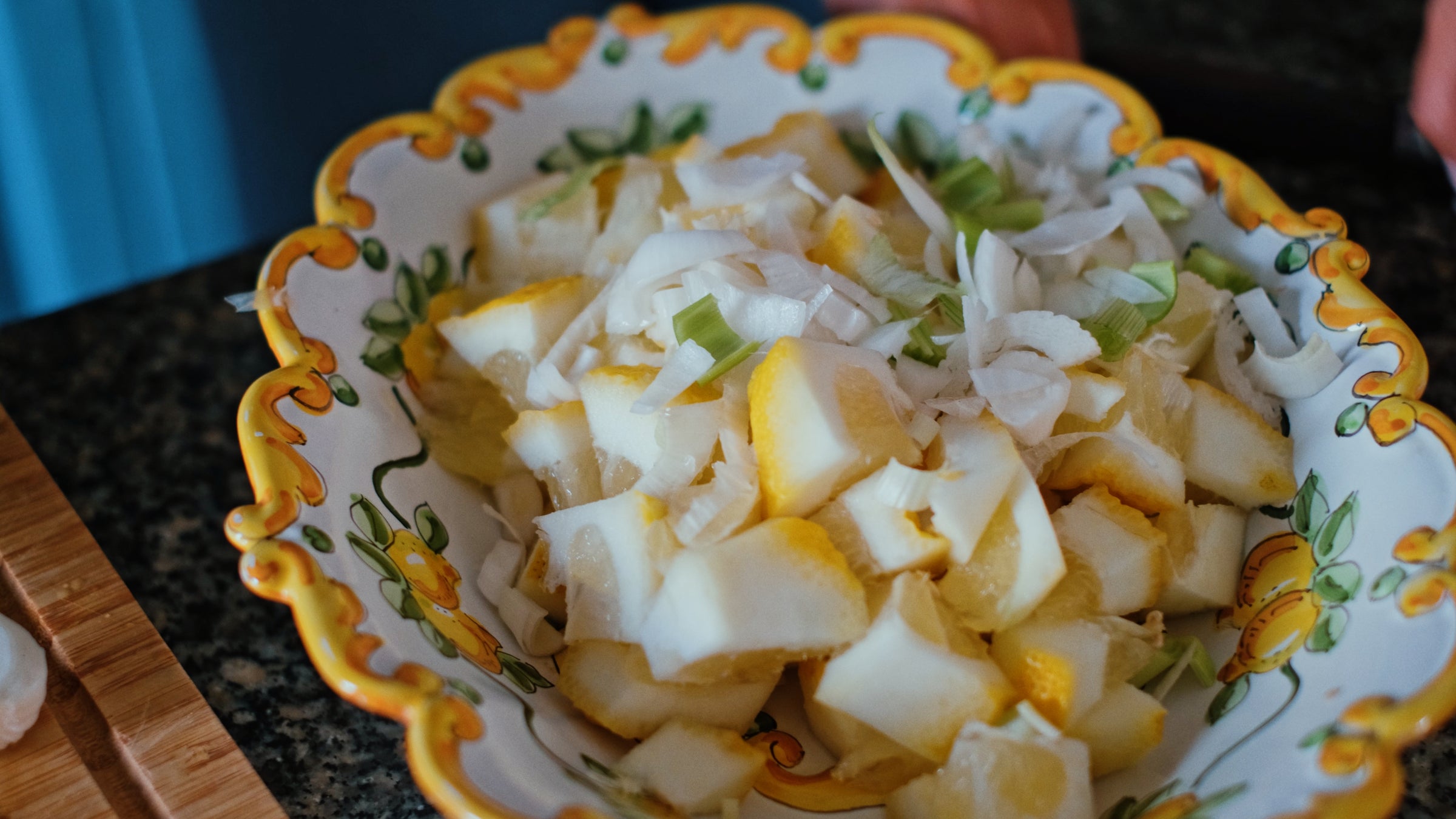 A decorative bowl filled with chopped yellow and white vegetables, including onions and what appears to be yellow squash, on a dark countertop.