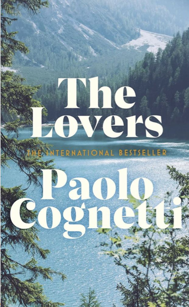 Book cover for The Lovers by Paolo Cognetti. White and gold text overlays a scenic view of a lake, pine trees, and forested mountains under a partly cloudy sky. Subheading reads The International Bestseller.
