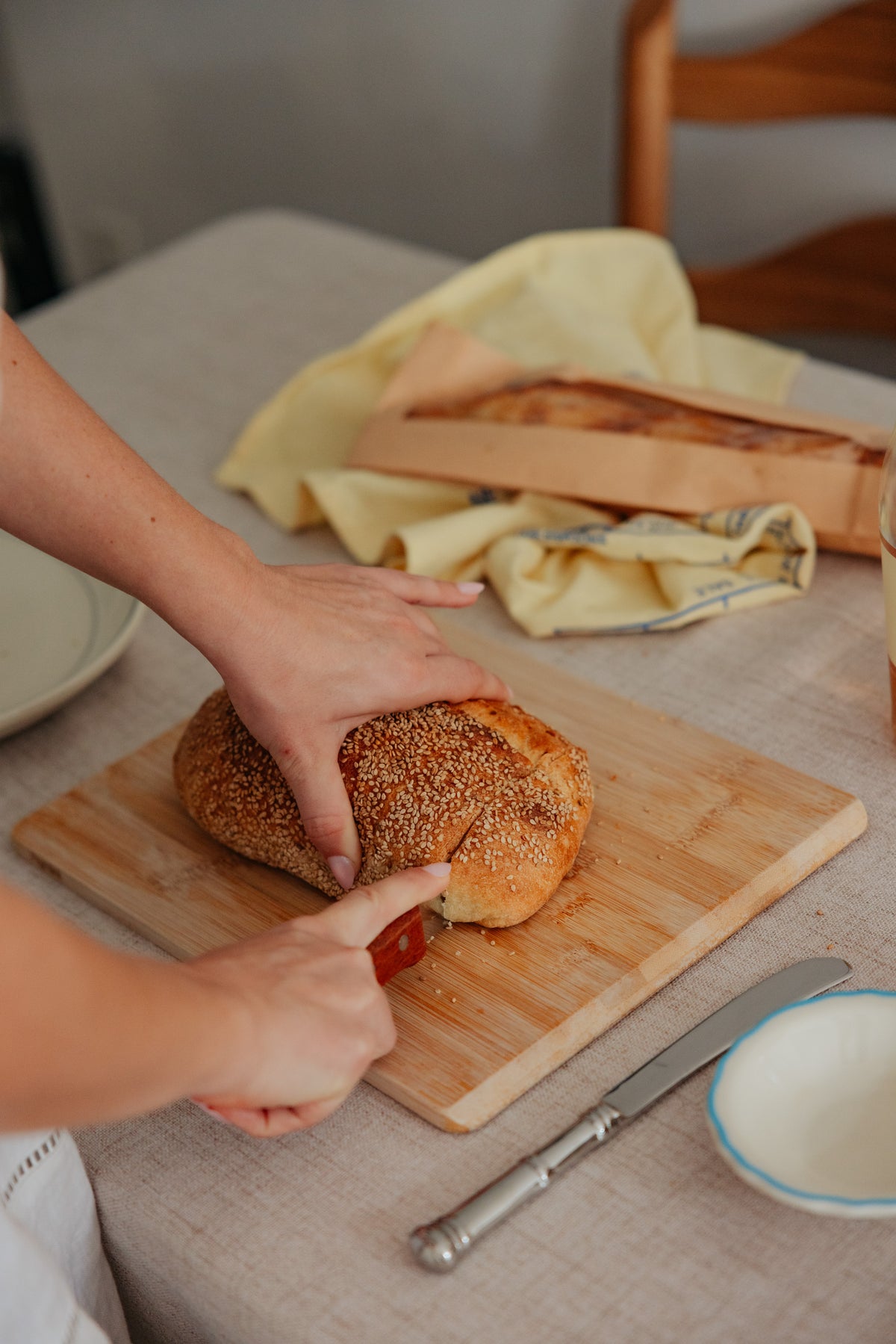 Hands slicing a loaf of sesame-crusted bread on a wooden cutting board.