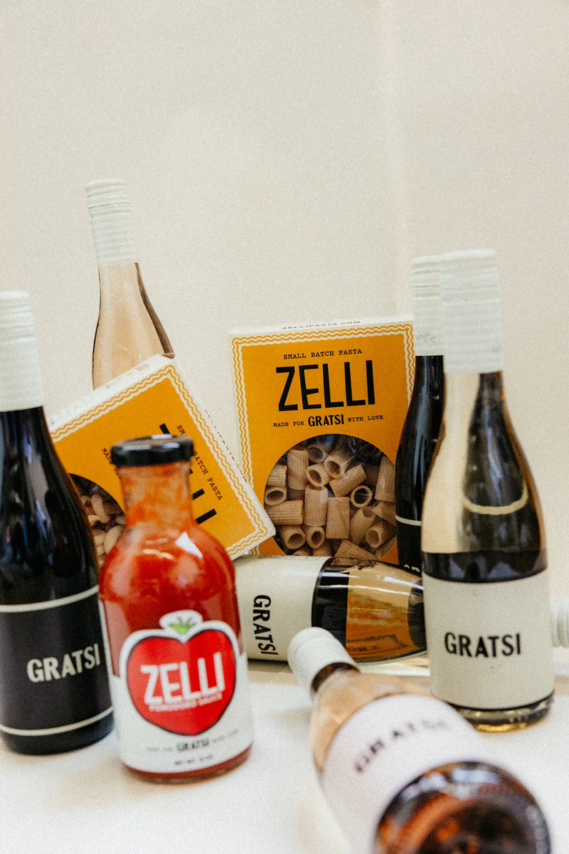 The Gratsi Wine & Pasta Holiday Bundle features bottles of Gratsi wine, Zelli tomato sauce, and Zelli pasta beautifully arranged on a white surface.