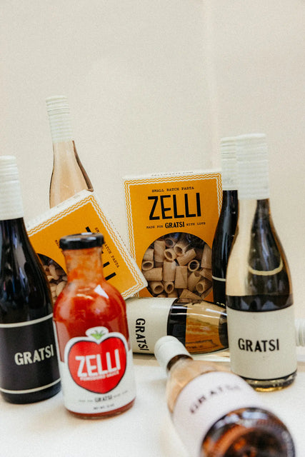 The Gratsi Wine & Pasta Holiday Bundle features bottles of Gratsi wine, Zelli tomato sauce, and Zelli pasta beautifully arranged on a white surface.