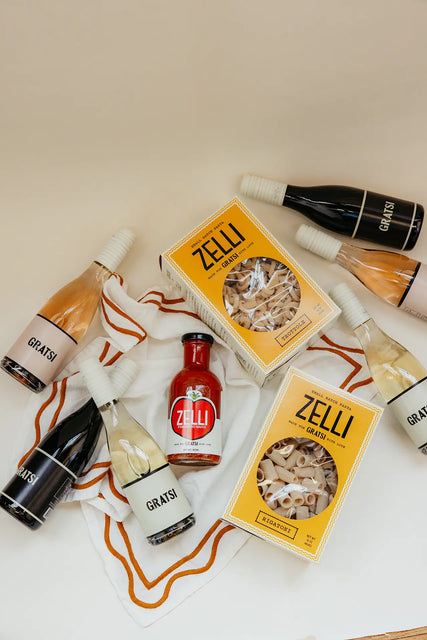 The Gratsi Wine & Pasta Holiday Bundle is displayed on a white cloth with orange trim, set against a beige background.