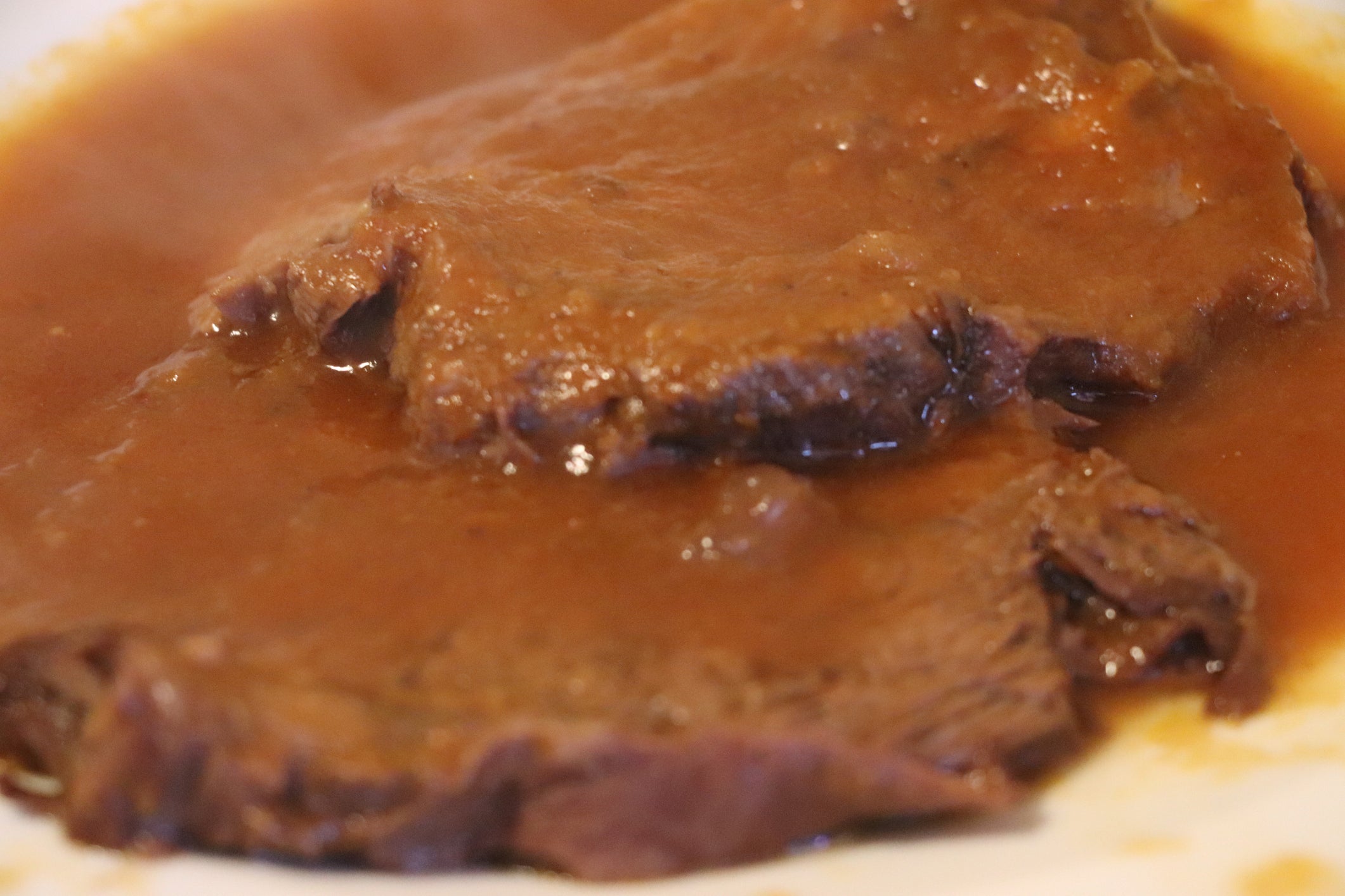Two slices of roast beef covered in brown gravy on a white plate.