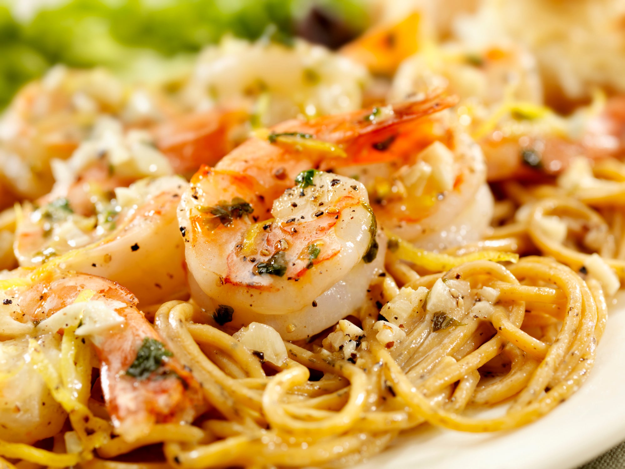 Close-up of shrimp scampi with spaghetti noodles, garnished with parsley and black pepper, and topped with garlic and lemon zest.