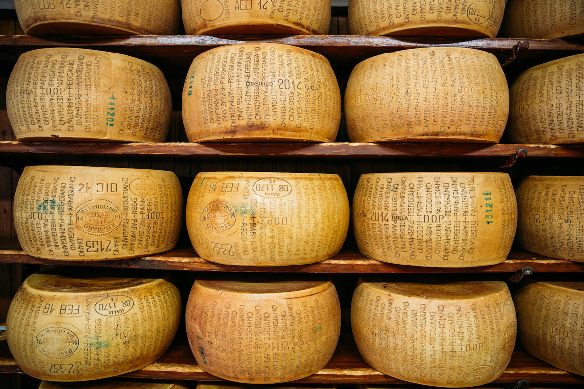 Large wheels of Parmigiano Reggiano cheese aging on wooden shelves, each wheel engraved with identifying stamps and marks.