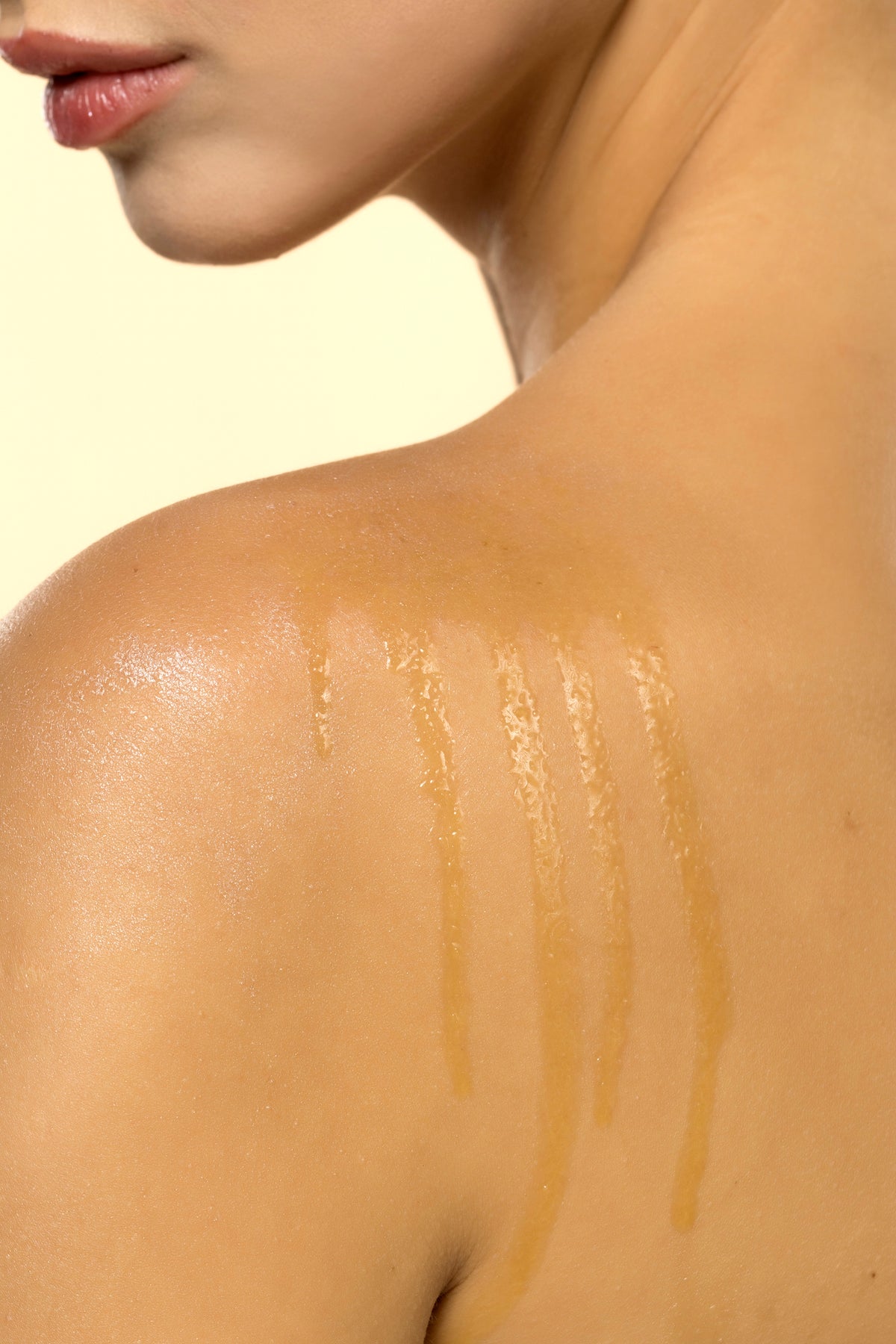 A close-up of a womans bare shoulder with three lines of honey drizzled on her skin, highlighting a skincare or beauty treatment.