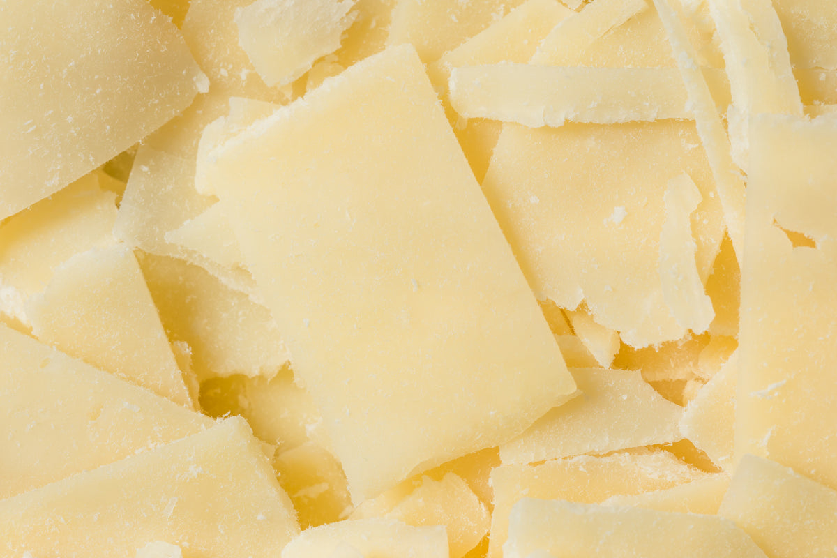 Close-up of several pale yellow, thin slices and shavings of hard cheese, showing rough edges and granular texture.