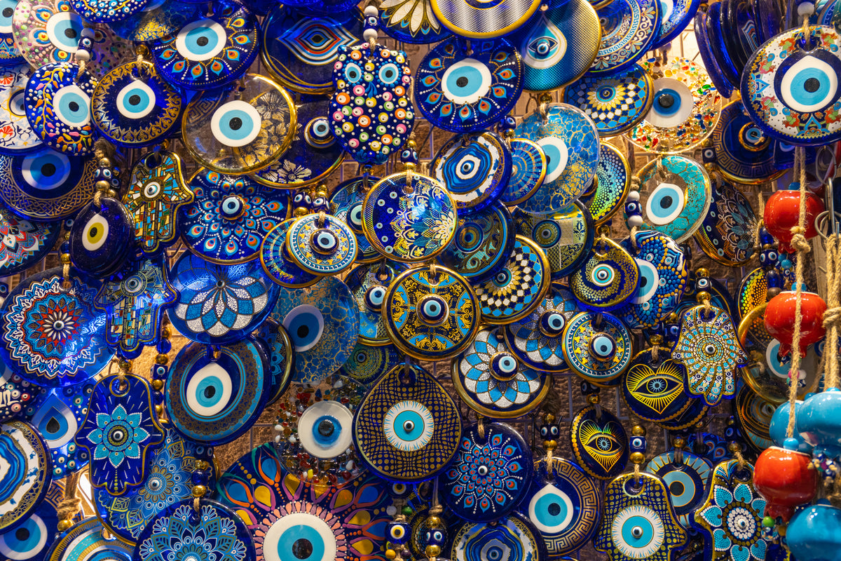 A collection of vibrant blue glass Nazar amulets, also known as evil eye charms, of various sizes and designs displayed closely together, creating a colorful and intricate mosaic pattern.