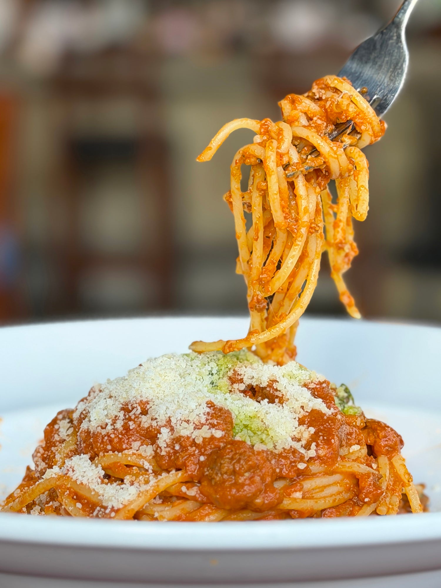A fork twirls spaghetti topped with tomato sauce and grated cheese on a white plate.