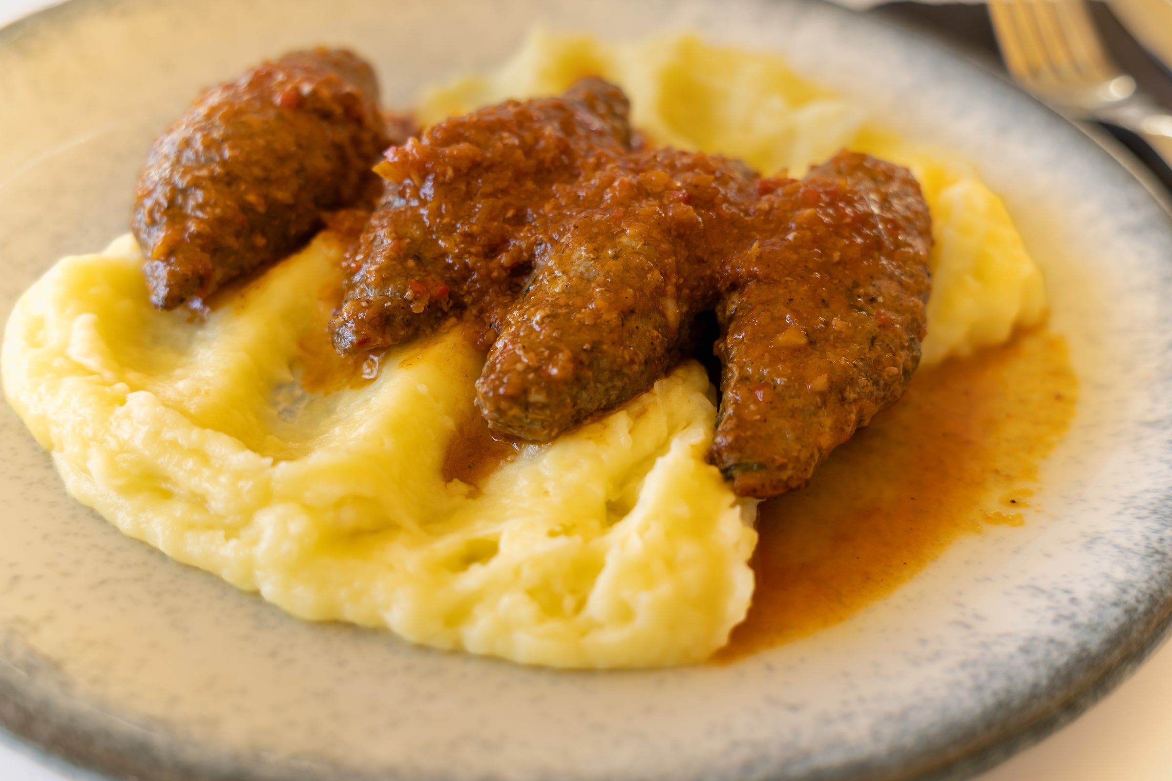 Three pieces of meatloaf topped with tomato sauce served on a bed of creamy mashed potatoes on a white plate.
