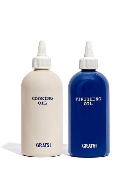 Two bottles from the Gratsi Oil Squeeze Bottle Set—one cream-colored labeled “COOKING OIL” and one blue labeled “FINISHING OIL,” both with Gratsi printed at the bottom.