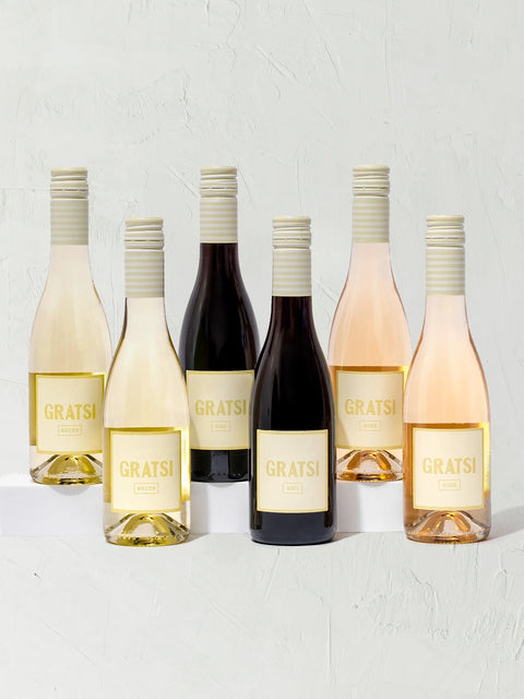 Six half bottles from the Gratsi Wine Sampler Kit + Glasses are arranged in two rows on a light textured background, showcasing an exclusive mix of white, rosé, and red wines with cream labels and striped screw caps.