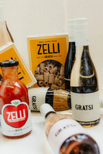 The Gratsi Wine & Pasta Valentine’s Bundle features Zelli Pasta and tomato sauce with Gratsi wine, all beautifully arranged on a light surface for an inviting gift set.